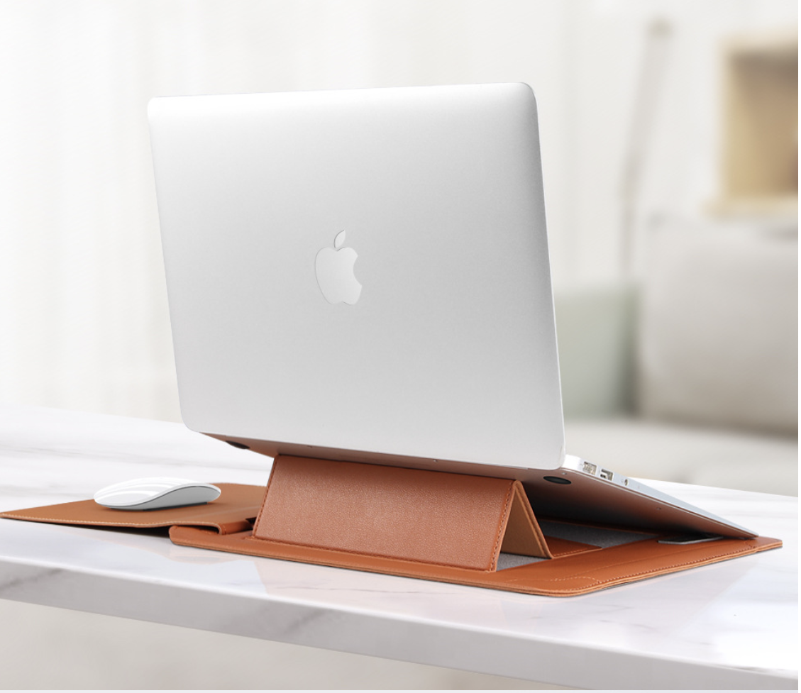 A brown leather laptop stand holding a silver Apple MacBook on a white marble desk, with a white mouse to the left and a softly blurred indoor background.